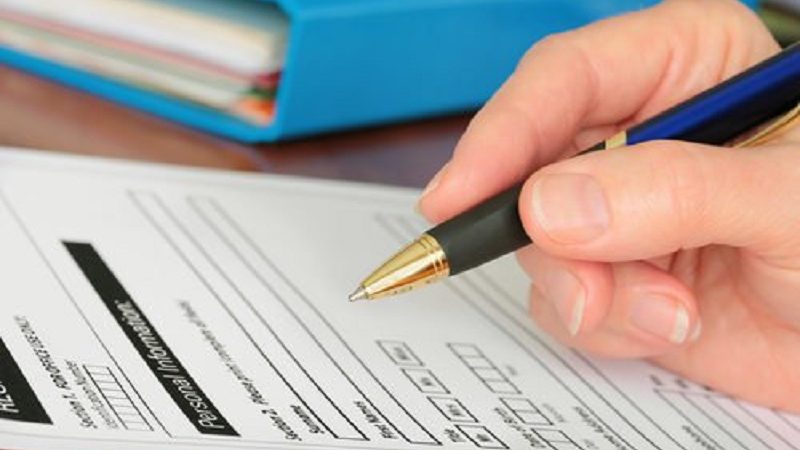 A hand holding a pen to an application form