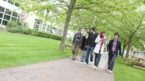 Students walking through green trees on Canterbury Campus - Laud building to the left